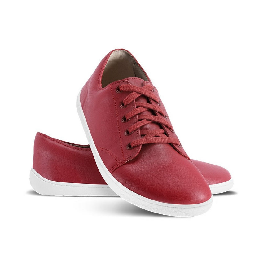 A photo of Jester Red Be Lenka Prime 2.0 Simple Leather Sneakers with white soles. Left shoe is shown from the right with the right shoe propped up on the left to show the top of the shoe. Background is white. #color_jester-red