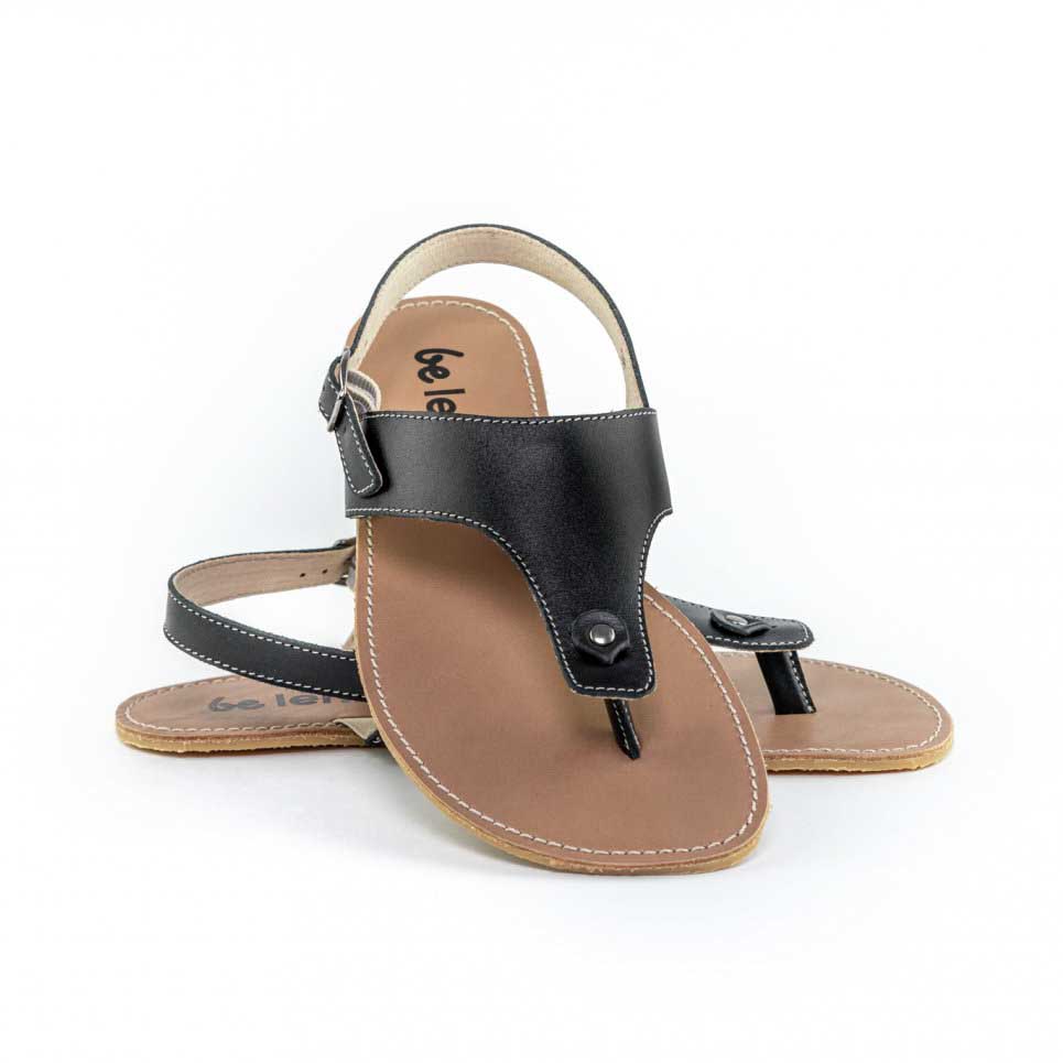 A photo of Black Be Lenka Promenade Sandals made with leather and tan rubber soles. The sandals have black thong straps and a heel strap with a buckle. The sandals are shown with the left sandal behind the right sandal. The right sandal is turned towards the front with its heel leaned on the left sandal against a white background in this photo. #color_black