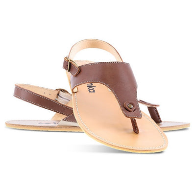A photo of Dark Brown Be Lenka Promenade Sandals made with leather and tan rubber soles. The sandals have dark brown thong straps and a heel strap with a buckle. The sandals are shown with the left sandal behind the right sandal. The right sandal is turned towards the front with its heel leaned on the left sandal against a white background in this photo. #color_dark-brown