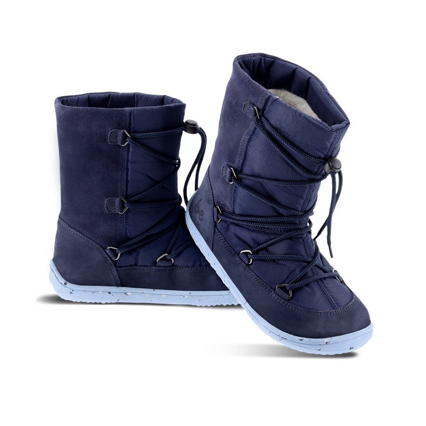 A photo of Be Lenka Kids Snowfox boots in dark and light blue. Dark blue suede and textile and light blue soles surround the outside. Dark blue laces are widely connected from side to side starting at the ball of the foot and going until the top of the boot with a quick lace connector securing the laces in place. Left shoe is shown from the left side with the right shoe heel proped up on the midfoot of the left shoe against a white background. #color_dark-light-blue
