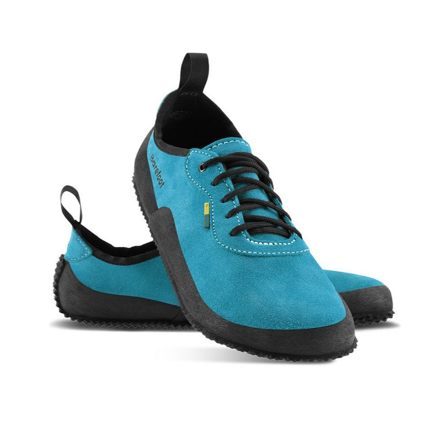 A photo of Be Lenka Trailwalkers 2.0 in Deep Ocean blue. Suede shoes are a low ankle height with black soles and laces, black rubber surrounding the lower part of the shoe, and pull/hook loops at the top of the heels. The top of the right shoe is shown tilted towards the camera here leaning on the left shoe pointing to the right against a white background. #color_deep-ocean