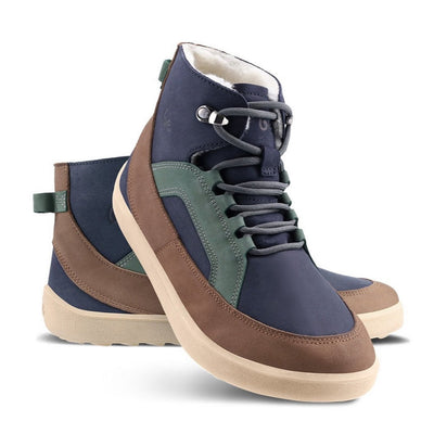 A photo of Be Lenka York ankle lace up boots made from nubuck leather and tan rubber soles. The boots have a navy base color with brown wrapped around the edge of the shoe up the back of the ankle, green angled arch detailing on either side of the laces, and grey laces. The left boot is shown from the right side with the right boot propped up against it with a white background. #color_navy-brown-beige