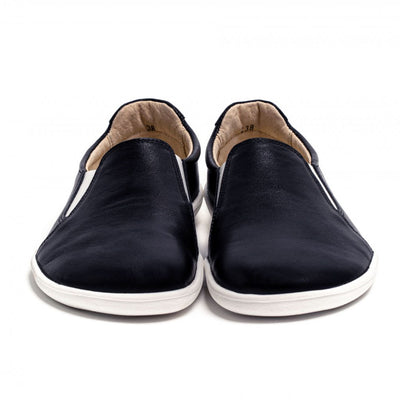 A photo of Belenka Eazy slip-on sneakers made from leather and rubber soles. The sneakers are a black color with white elastic on the sides and soles. Both shoes are shown from the front against a white background. #color_black