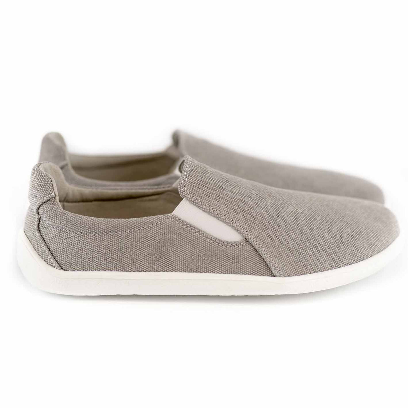 A photo of Belenka Eazy slip-on sneakers made from canvas and rubber soles. The sneakers are a sand color with white elastic on the sides and soles. Both shoes are shown beside each other facing towards the left against a white background. #color_sand