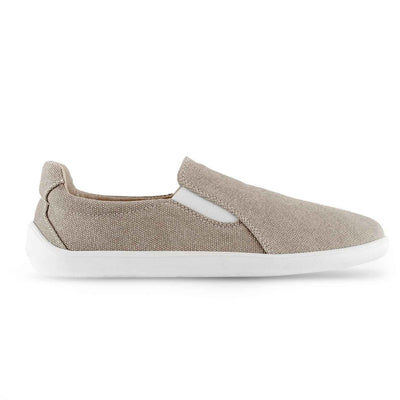 A photo of Belenka Eazy slip-on sneakers made from canvas and rubber soles. The sneakers are a sand color with white elastic on the sides and soles. The left shoe is shown from the right side against a white background. #color_sand