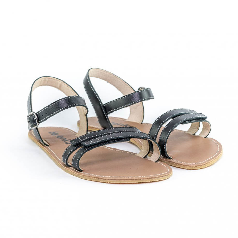 A photo of Black Be Lenka Summer Sandals made with leather and tan rubber soles. The sandals are black and have thin double straps on the front of the foot. They also have straps that go around the ankle and heel and have a small buckle. Both sandals are shown beside each other facing forward and slightly angled to the right against a white background. color_black