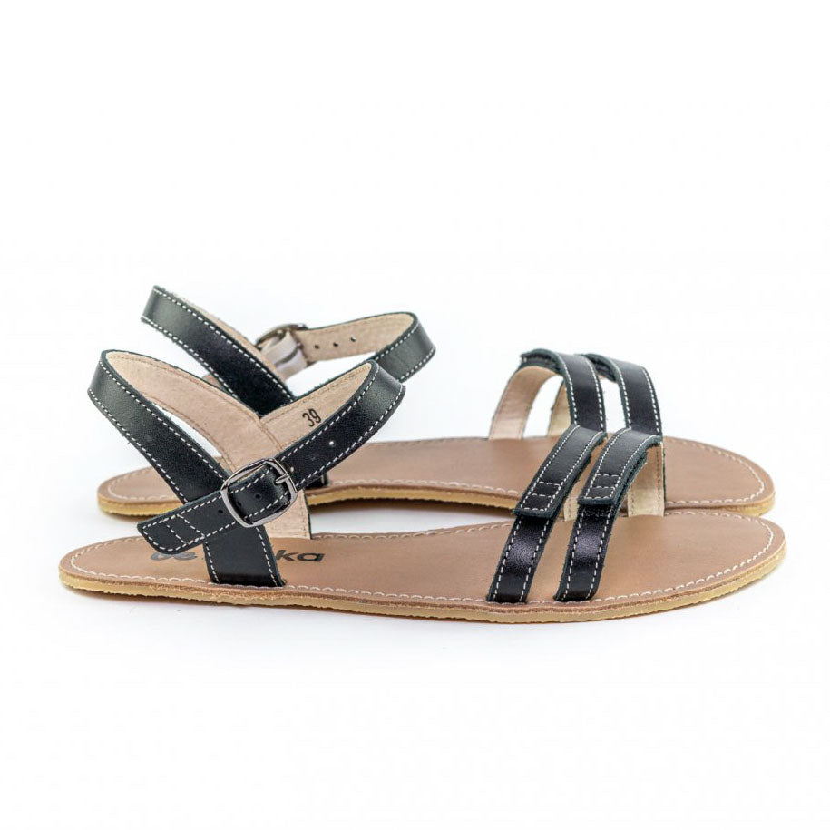 A photo of Black Be Lenka Summer Sandals made with leather and tan rubber soles. The sandals are black and have thin double straps on the front of the foot. They also have straps that go around the ankle and heel and have a small buckle. Both sandals are shown from the right side against a white background in this photo. #color_black