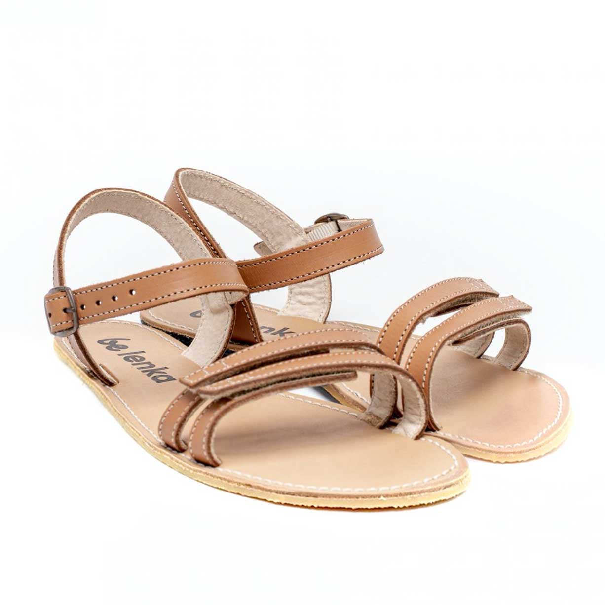 A photo of Brown Be Lenka Summer Sandals made with leather and tan rubber soles. The sandals are medium brown in color and have thin double straps on the front of the foot. They also have straps that go around the ankle and heel and have a small buckle. Both sandals are shown beside each other on the right side and angled slightly to the front against a white background. #color_brown