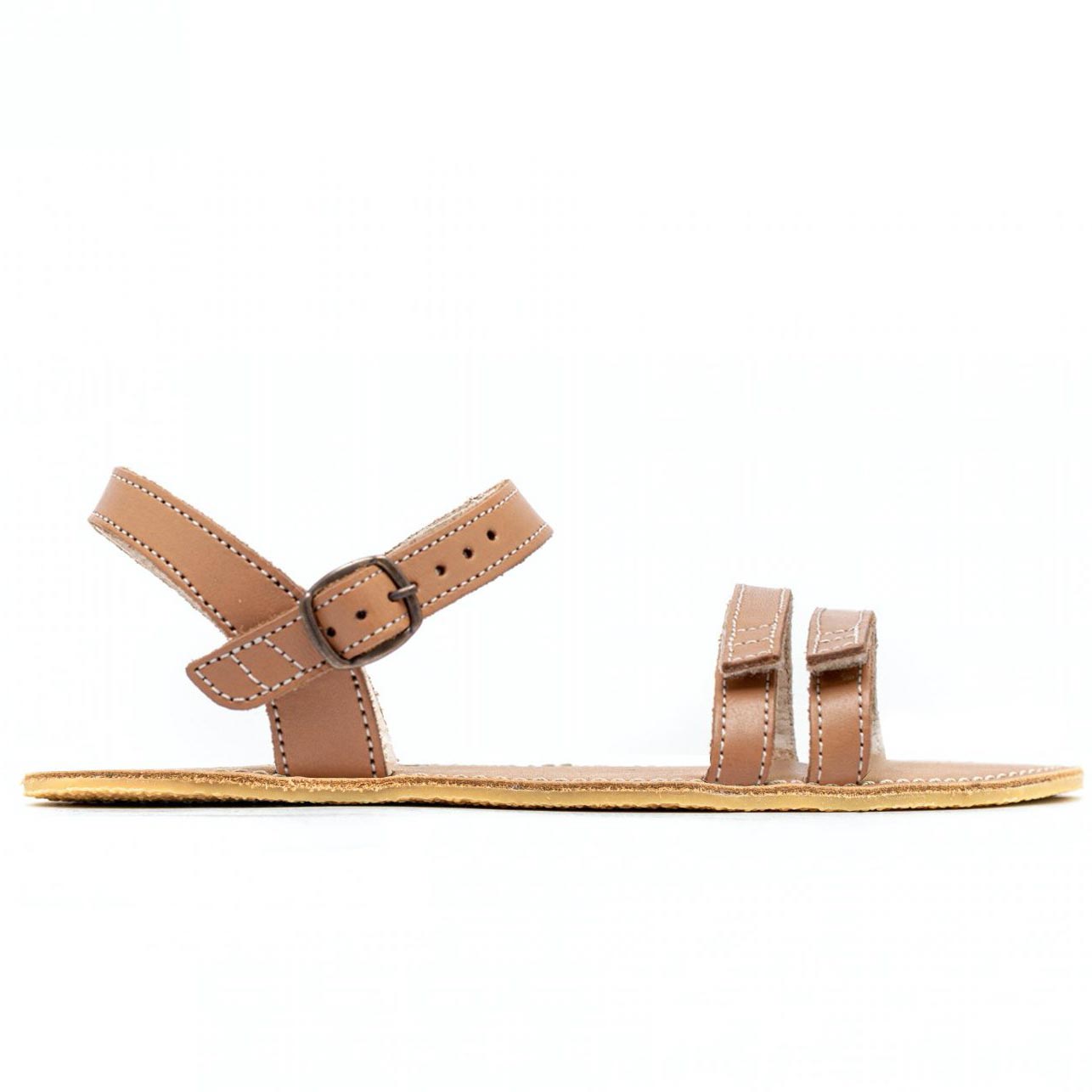 A photo of Brown Be Lenka Summer Sandals made with leather and tan rubber soles. The sandals are medium brown in color and have thin double straps on the front of the foot. They also have straps that go around the ankle and heel and have a small buckle. One sandal is shown from the right side against a white background in this photo. #color_brown