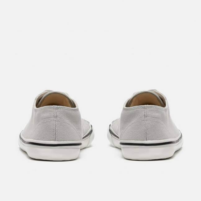 A photo of Bohempia Herlik canvas sneakers made from canvas and rubber soles. The sneakers are light grey with a white toe cap and a black outline around the white rubber soles. Both sneakers are shown from behind on a white background. #color_light-grey-white