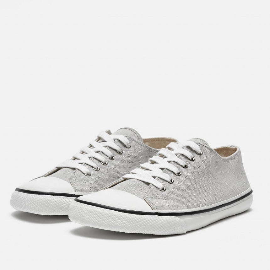 A photo of Bohempia Herlik canvas sneakers made from canvas and rubber soles. The sneakers are light grey with a white toe cap and a black outline around the white rubber soles. Both sneakers are shown from the front left on a white background. #color_light-grey-white