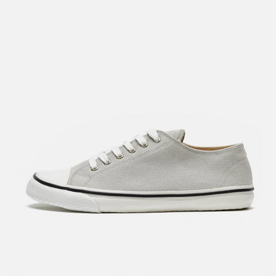 A photo of Bohempia Herlik canvas sneakers made from canvas and rubber soles. The sneakers are light grey with a white toe cap and a black outline around the white rubber soles. The left sneaker is shown from the left side against a white background. #color_light-grey-white