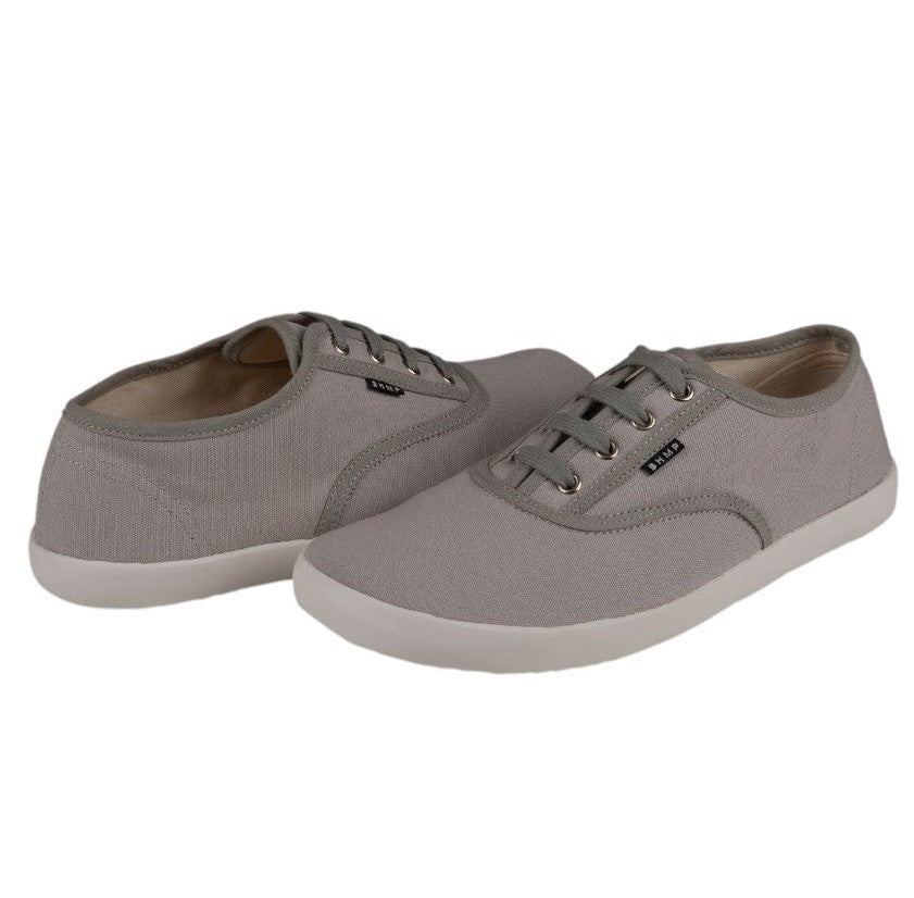 A photo of Bohempia Kolda Plimsole sneakers made from canvas and rubber soles. The sneakers are grey in color with trim detailing and a small tag on the top by the laces.  Both shoes are shown in opposite directions each other, the left shoe is facing towards the front and the right shoe is facing towards the back against a white background. #color_grey