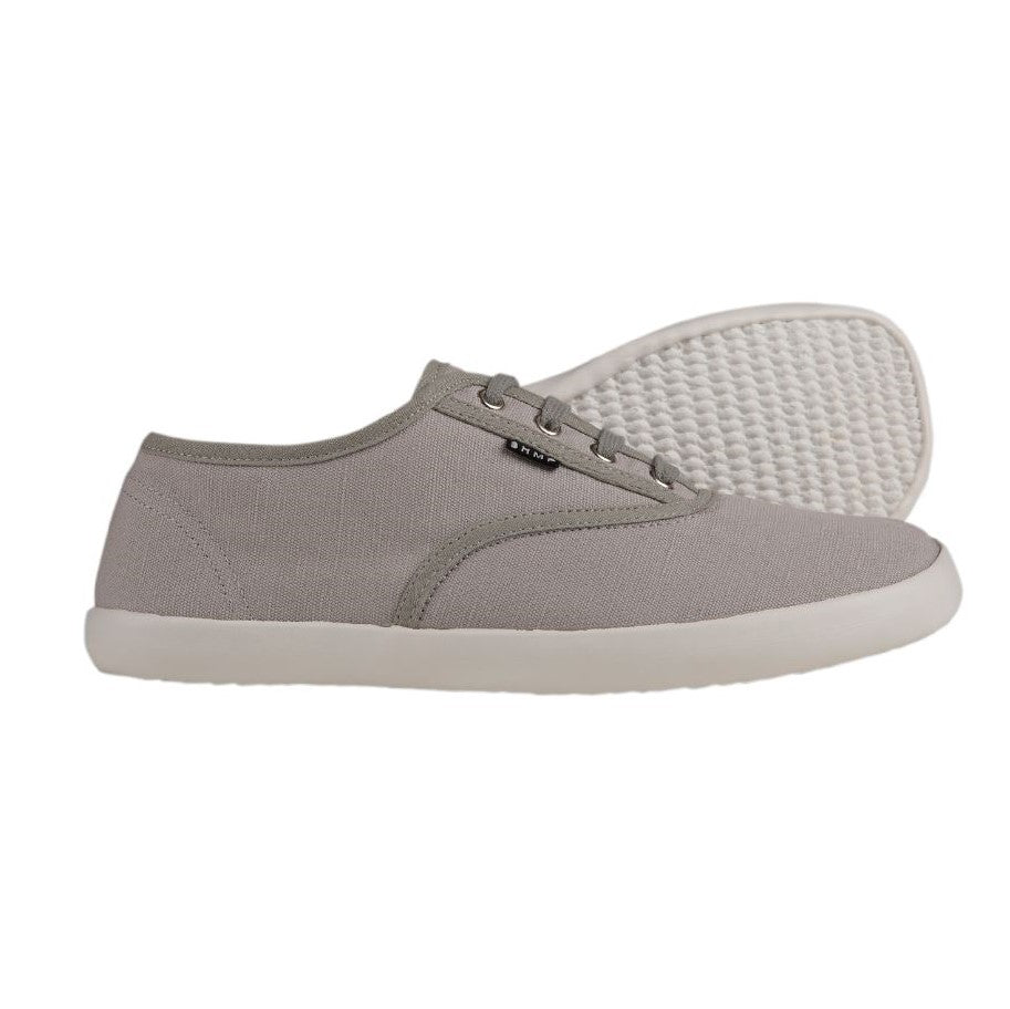 A photo of Bohempia Kolda Plimsole sneakers made from canvas and rubber soles. The sneakers are grey in color with trim detailing and a small tag on the top by the laces. Both shoes are shown beside each other the right shoe is in front facing towards the right and the left shoe is shown behind the right shoe laying on it’s side with the sole towards the front against a white background. #color_grey
