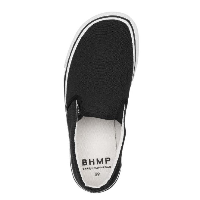 A photo of Bohempia Velik slip on sneakers made from canvas and rubber soles. The sneakers are a black color and white soles with a black stripe around the sole. The left shoe is shown from the top against a white background. #color_black-white