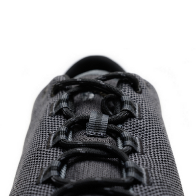 A photo of Freet Pace sneakers in charcoal. Sneakers are completely knit and have a detatched tongue. Laces are black and loop through fabric tabs attached to the shoe and a tab on the tongue. The right shoe is shown here from the front laces against a white background. #color_charcoal