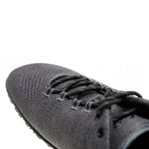 A photo of Freet Pace sneakers in charcoal. Sneakers are completely knit and have a detatched tongue. Laces are black and loop through fabric tabs attached to the shoe and a tab on the tongue. The right shoe is shown here diagonally from the back left against a white background. #color_charcoal