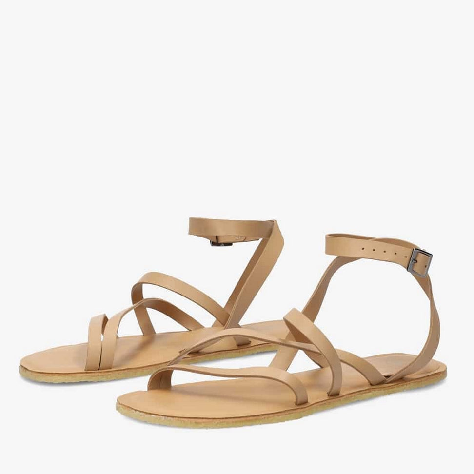 A photo of beige leather Groundies Florence Sandals. Two leather straps start at the ball of the big toe with one ending at the ball of the little toe and the other midfoot. Another strap goes from one side of the heel over the top of the foot to the other side with one final strap wrapping around the ankle and closing with a buckle. Shoes are shown diagonally from the front left side against a white background. #color_beige