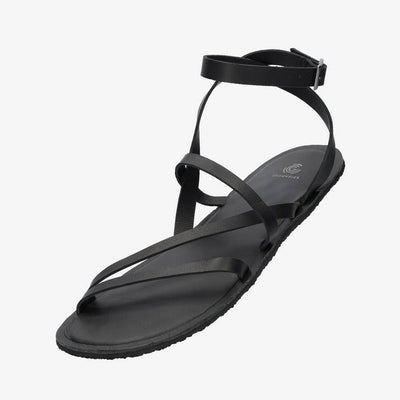 A photo of black leather Groundies Florence Sandals. Two leather straps start at the ball of the big toe with one ending at the ball of the little toe and the other midfoot. Another strap goes from one side of the heel over the top of the foot to the other side with one final strap wrapping around the ankle and closing with a buckle. Shoe is shown floating diagonally from the front left side against a white background. #color_black