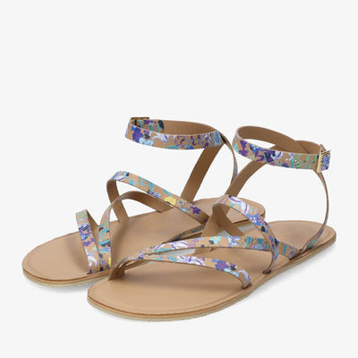 A photo of beige leather Groundies Florence Sandals with blue and white flower details. Two leather straps start at the ball of the big toe with one ending at the ball of the little toe and the other midfoot. Another strap goes from one side of the heel over the top of the foot to the other side with one final strap wrapping around the ankle and closing with a buckle. Both shoes are shown diagonally from the front left side against a white background. #color_beige