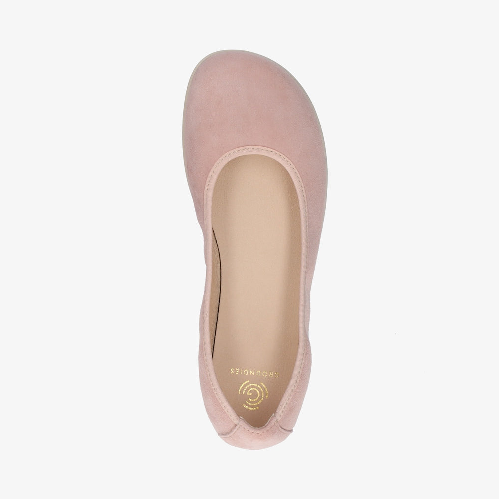 A photo of Groundies Lily Soft flats with a leather upper and cream rubber true sense soles. The flats are a nubuck in a light pink color, the trim around the tops of the flats is a light pink color that is lighter than the rest of the flats. The interior of the flats is a light beige color. The right flat is shown floating facing downwards against a white background. #color_light-pink