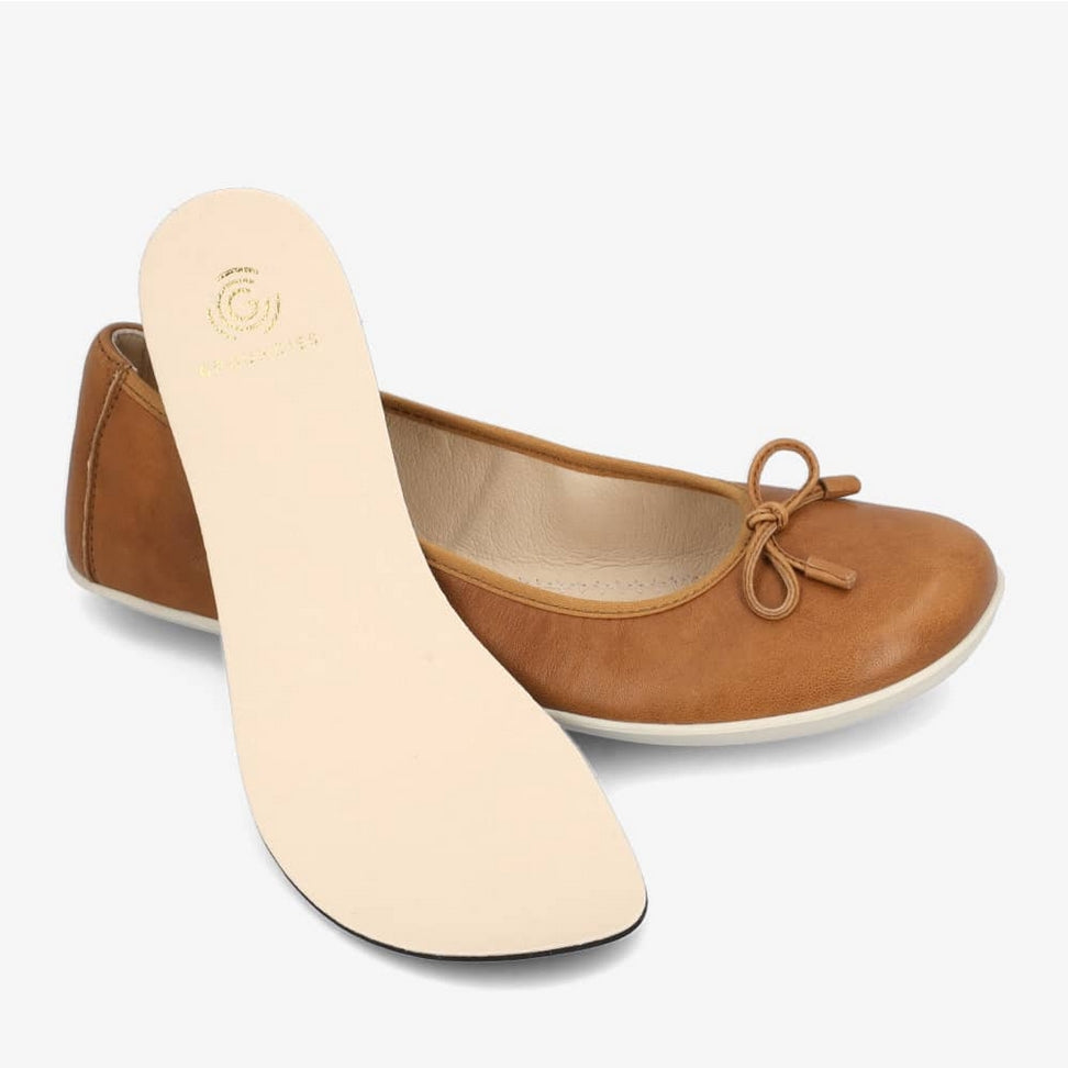 A photo of light brown leather Groundies Magnolia Flats. These classic ballet flats are simple with a leather bow located at the top of the shoe opening. Right shoe is shown from the right side with the removeable insole out and resting diagonally on the shoe against a white background. #color_light-brown