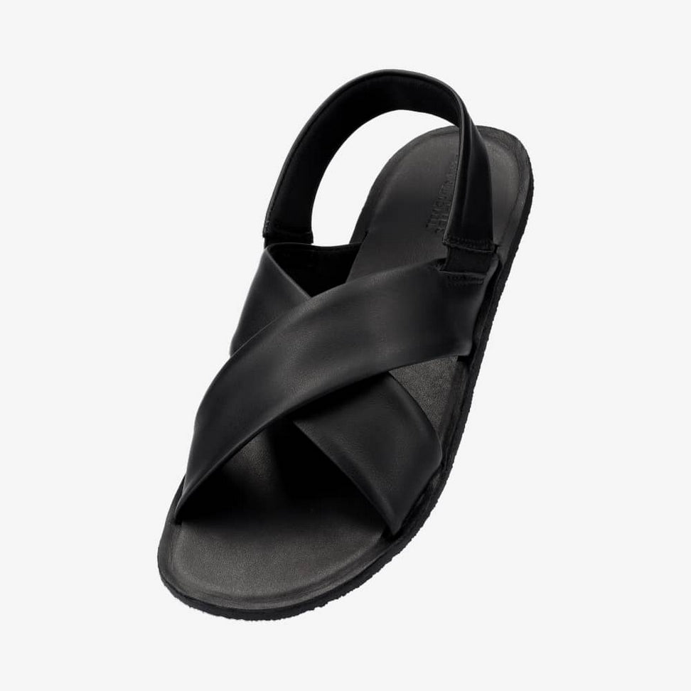 Photo 1 - A photo of Groundies Verona leather sandals in black. Two thick straps make an X across the foot while a thinner strap keeps the sandal secure to the foot. The right shoe is shown from the right against a white background. Photo 2 - Left shoe is shown floating diagonally from the left against a white background.  #color_black