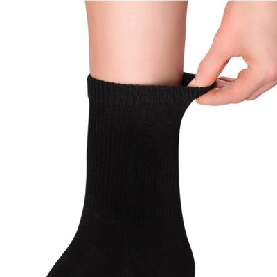 A photo of Knitido essential midi crew toe socks made with cotton, nylon, and elastane. The socks are a black color. A woman’s leg is shown mid leg to ankle wearing the black crew socks while she holds the elastic at the top out slightly against a white background. #color_black