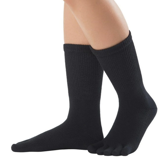 A photo of Knitido merino wool crew toe socks made with wool, nylon, and elastane. The socks are black in color. A woman is shown from the mid calf down wearing the black crew toe socks, she is facing left and has one heel lifted slightly off the ground against a white background. #color_black