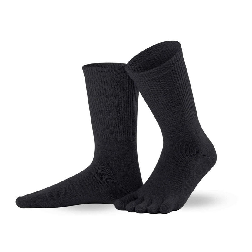A photo of Knitido merino wool crew toe socks made with wool, nylon, and elastane. The socks are black in color. Both socks are shown beside each other facing to the left side, the left sock is slightly behind the right with it’s heel lifted off the ground against a white background. #color_black