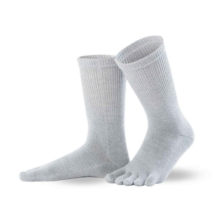 A photo of Knitido merino wool crew toe socks made with wool, nylon, and elastane. The socks are light grey in color. Both socks are shown beside each other facing to the left side, the left sock is slightly behind the right with it’s heel lifted off the ground against a white background. #color_light-grey