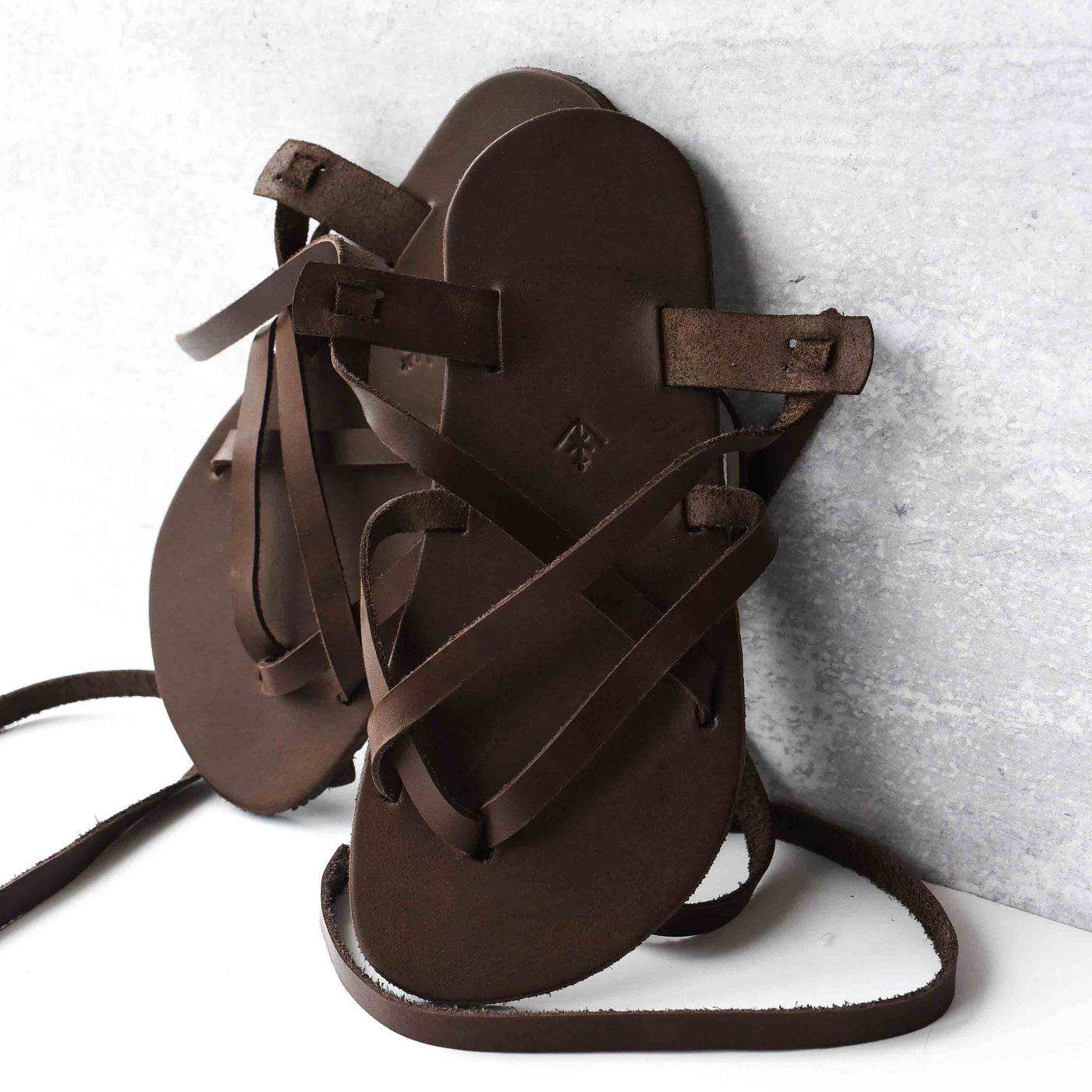 a brown leather strappy sandal shown propped up on a white wall #color_brown