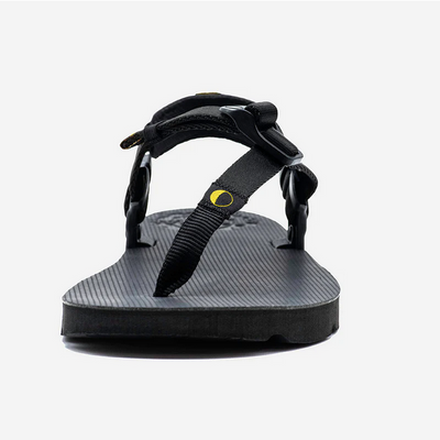A photo of Luna Mono Winged Black Adventure Sandals made from a monkey grip technology footbed and a rubber sole. The sandals have a thong toe strap with straps that go around the ankle and heel. The sandals have a logo moon on the thong toe strap and luna logo on the heel and right ankle strap. The left sandal is shown from the front against a white background. #color_black