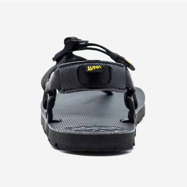 A photo of Luna Mono Winged Black Adventure Sandals made from a monkey grip technology footbed and a rubber sole. The sandals have a thong toe strap with straps that go around the ankle and heel. The sandals have a logo moon on the thong toe strap and luna logo on the heel and right ankle strap. The sandal is shown from the back against a white background. #color_black