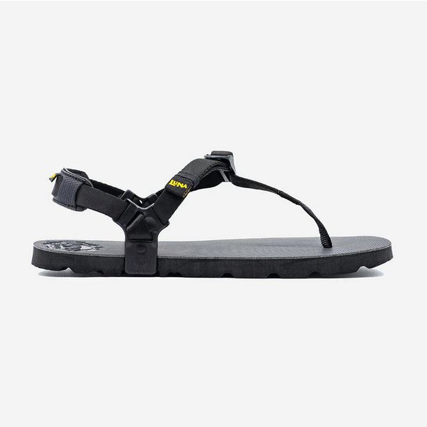 A photo of Luna Mono Winged Black Adventure Sandals made from a monkey grip technology footbed and a rubber sole. The sandals have a thong toe strap with straps that go around the ankle and heel. The sandals have a logo moon on the thong toe strap and luna logo on the heel and right ankle strap. The left sandal is shown from the right side against a white background.  #color_black