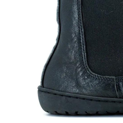 A photo of Mukishoes felted-wool-lined, leather Chelsea boots in black. Boots have elastic pannels on both sides of the shoe and a pull tab at the top of the ankle opening. Soles are black in color and are stitched to the leather. The right boot sole and heel is shown close up here diagonally from the right side against a white background. #color_black