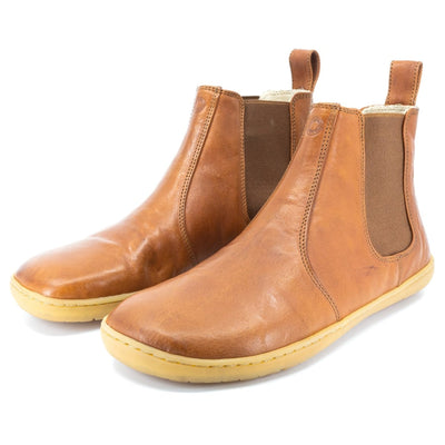 A photo of Mukishoes felted-wool-lined, leather Chelsea boots in caramel. Boots have brown elastic pannels on both sides of the shoe and a pull tab at the top of the ankle opening. Soles are a natural gum rubber color and are stitched to the leather. Both boots are shown here diagonally  from the front left side against a white background. #color_caramel