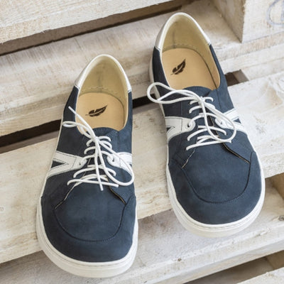 A photo of navy blue Peerko Street sneakers made with leather and recyclable soles. White pointed A-shaped detail present on both sides. Both shoes are shown from the front on top of light wooden steps. #color_navy