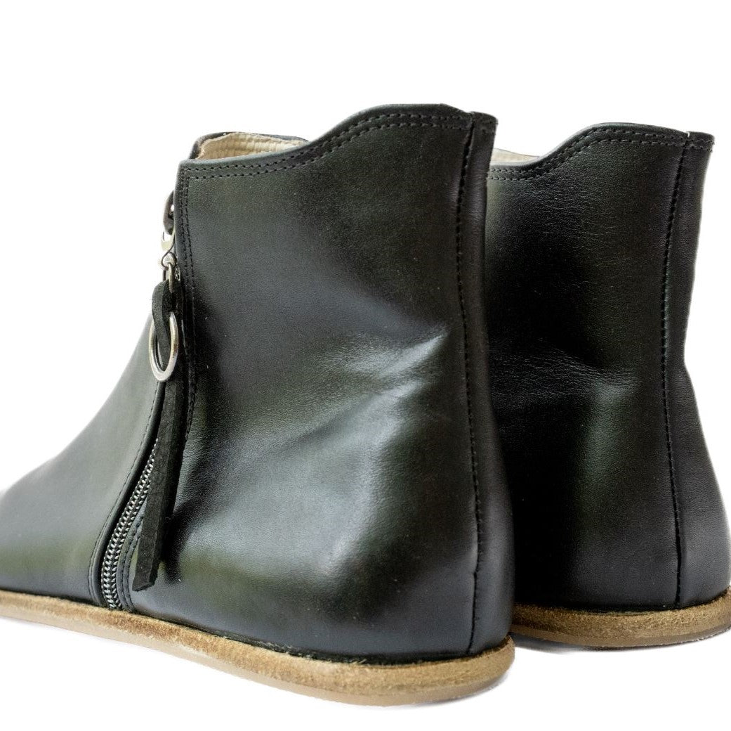 A photo of designed by Anya Rosa boots made from leather and rubber soles. The boots are black in color, they are a Chelsea boot style with a zipper on the sides. Both boots are shown beside each other up close from the back heel against a white background. #color_black-smooth-leather