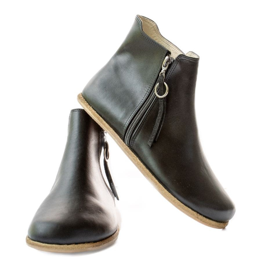 A photo of designed by Anya Rosa boots made from leather and rubber soles. The boots are black in color, they are a Chelsea boot style with a zipper on the sides. Both boots are shown the right boot is shown from the front angled slightly to the left, the heel of the is resting on the left boot and facing downward against a white background. #color_black-smooth-leather