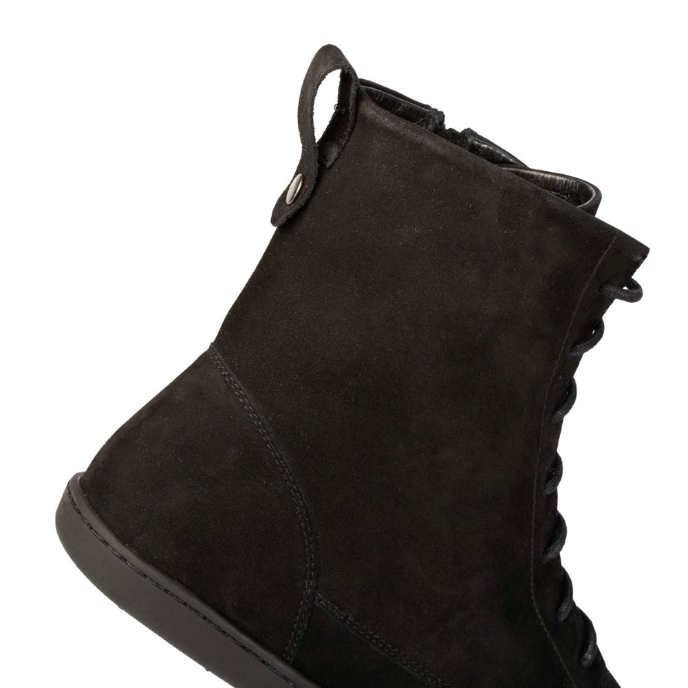 A photo of the Shapen Cozy lace up boots made from a water resistant nubuck leather upper, wool lining, and blacck rubber soles. The boots are black in color with black laces and have a zipper on the inner side. The right boot is shown from the right side focused on the top back of the boot where there is a leather tab to assist in pulling the shoes on, on a white background. #color_black