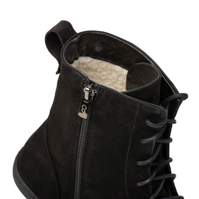 A photo of the Shapen Cozy lace up boots made from a water resistant nubuck leather upper, wool lining, and black rubber soles. The boots are black in color with black laces and have a zipper on the inner side. The left boot is shown from the top focused on the opening of the boot to show the wool lining and the zipper up close, on a white background. #color_black