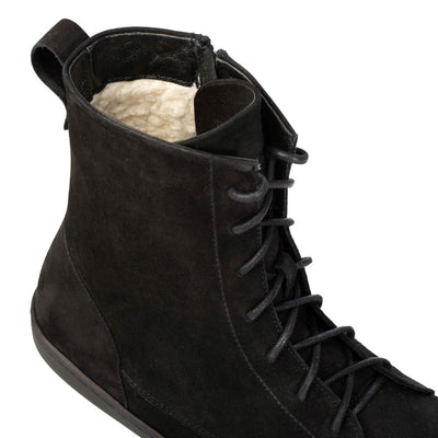 A photo of the Shapen Cozy lace up boots made from a water resistant nubuck leather upper, wool lining, and black rubber soles. The boots are black in color with black laces and have a zipper on the inner side. The right boot is shown from the top focused on the opening of the boot to show the wool lining and the laces up close, on a white background. #color_black
