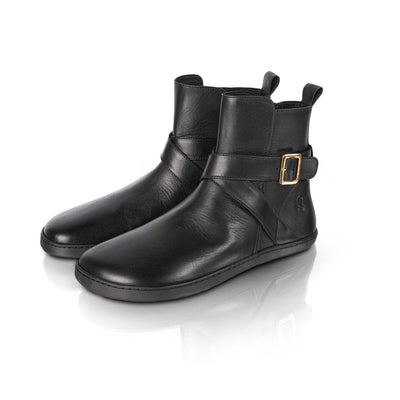 A photo of the Shapen Divine ankle boots made with a smooth leather upper, a microline lining, and rubber soles. The boots are black in color and have an ankle strap with a gold buckle, as well as a side zipper. Both boots are shown together from the front left on a white background. #color_black
