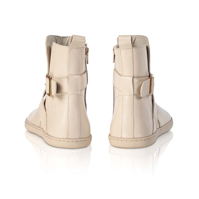 A photo of the Shapen Divine ankle boots made with a smooth leather upper, a microline lining, and rubber soles. The boots are vanilla in color and have an ankle strap with a gold buckle, as well as a side zipper. Both boots are shown from behind on a white background. #color_vanilla