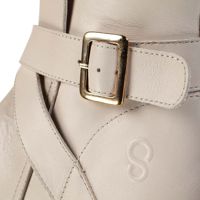 A photo of the Shapen Divine ankle boots made with a smooth leather upper, a microline lining, and rubber soles. The boots are vanilla in color and have an ankle strap with a gold buckle, as well as a side zipper. The left boot is shown with a closeup of the buckle detail on a white background. #color_vanilla