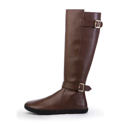 A photo of Shapen Glam lined riding boots made with vegan leather a faux fur lining and rubber soles. The boots are brown in color with gold buckles on the top and around the ankle, the ankle buckle strap is removable. One boot is shown from the left side against a white background. #color_brown