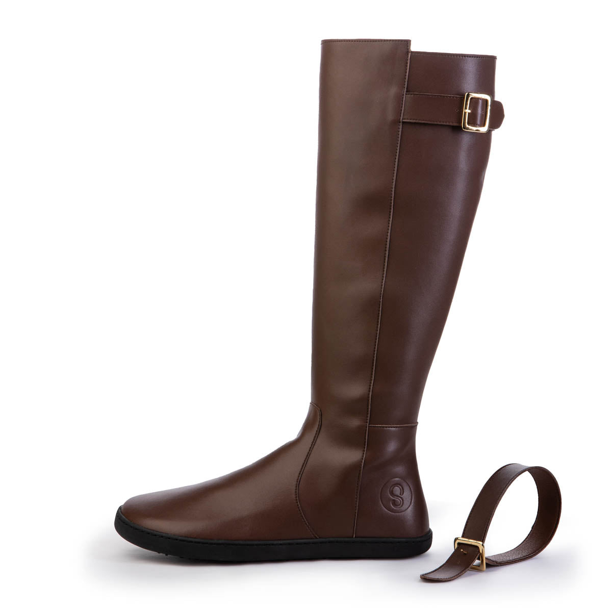 A photo of Shapen Glam lined riding boots made with vegan leather a faux fur lining and rubber soles. The boots are brown in color with gold buckles on the top and around the ankle, the ankle buckle strap is removable. One boot is shown from the left side with the ankle buckle strap removed against a white background. color_brown