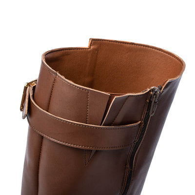 A photo of Shapen Glam lined riding boots made with leather a faux fur lining and rubber soles. The boots are brown in color with zippers on the side and gold buckles on the top and around the ankle, the ankle buckle strap is removable. An up close shot is shown off the top of the boots to show the detail against a white background. #color_brown