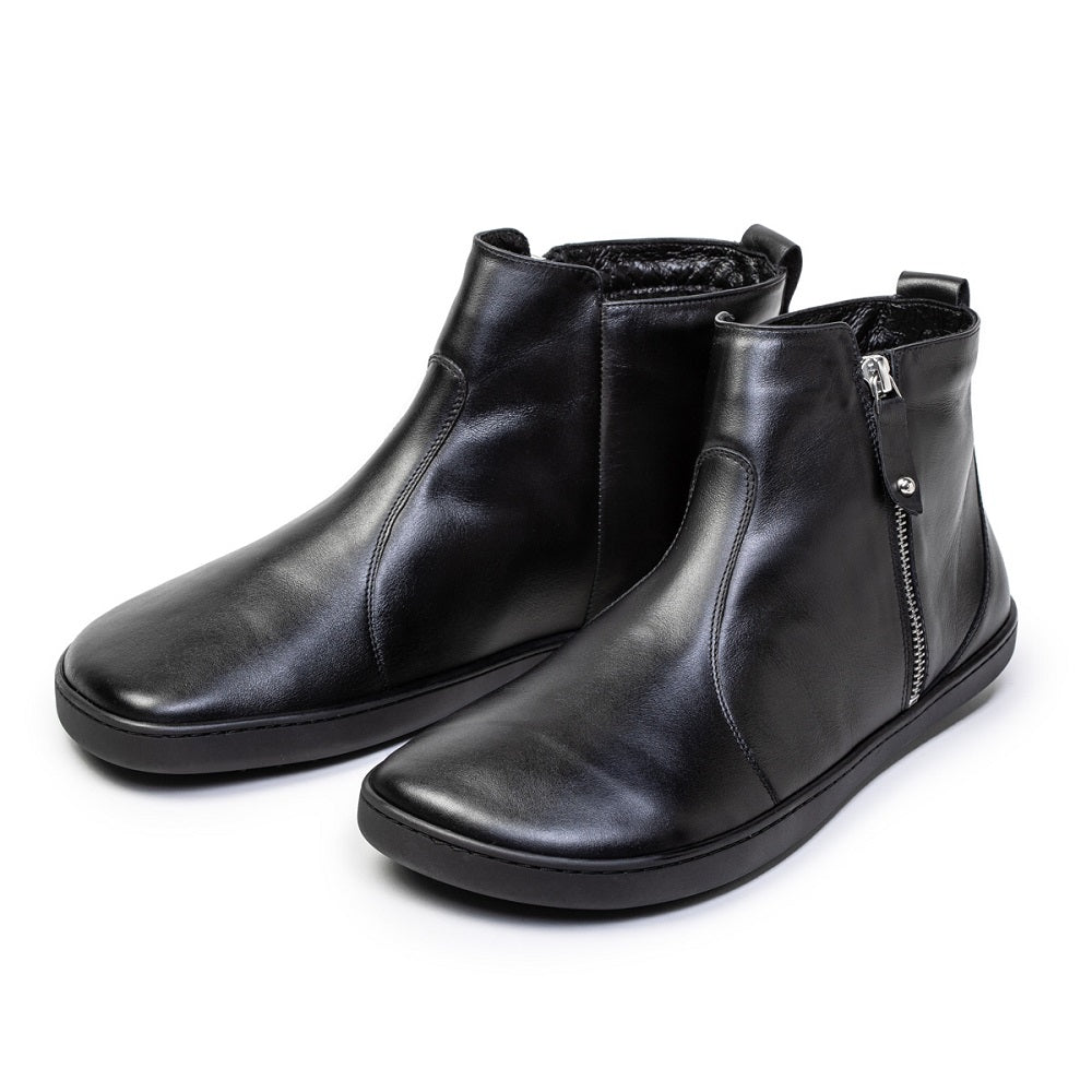 A photo of Shapen Ivy Chelsea boots made from smooth leather and rubber soles. The boots are black in color with stitching detailing and have a silver zipper with a leather tab on the side. Both boots are shown beside each other facing forward angled slightly to the right side against a white background. #color_black